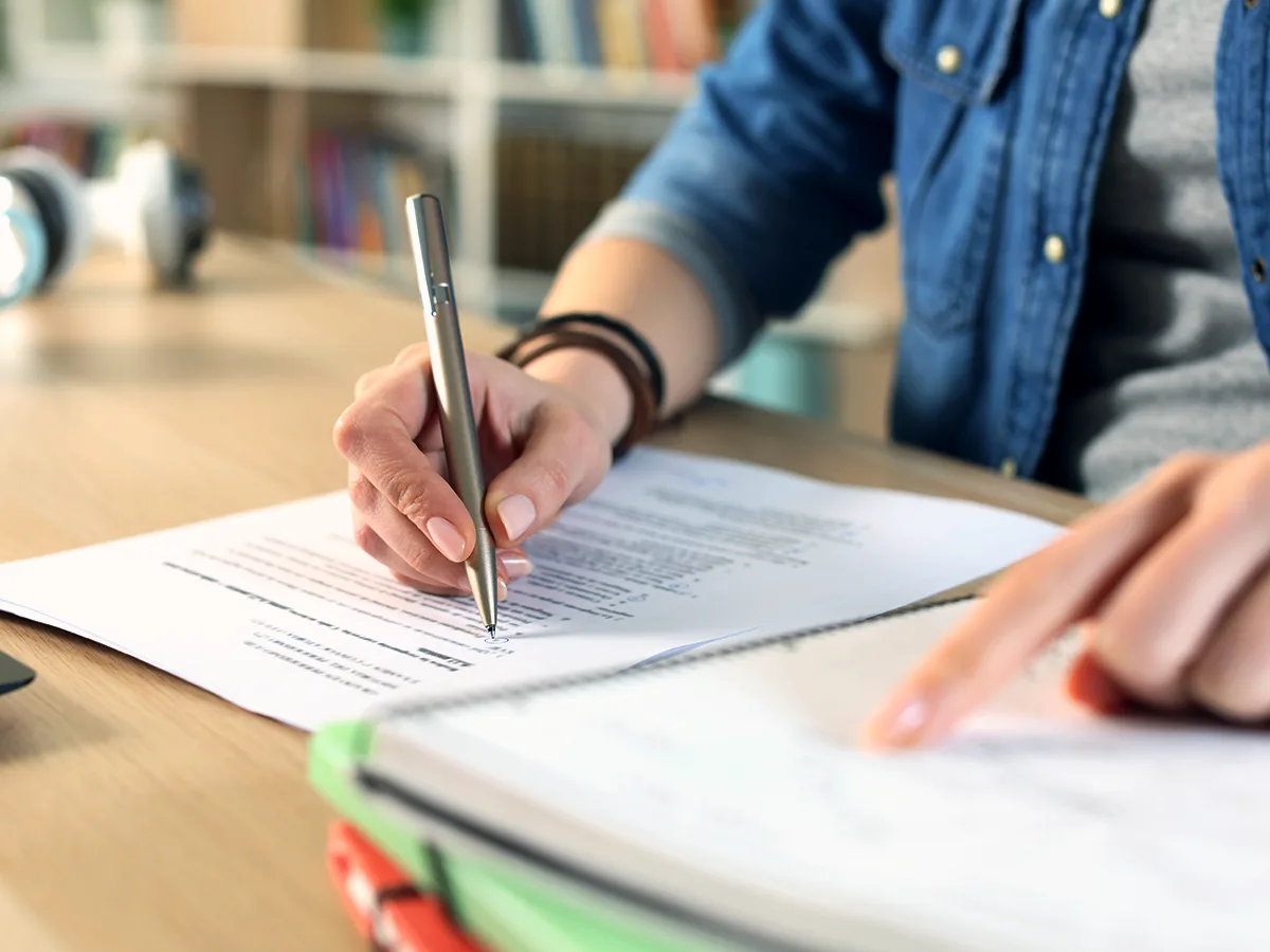 Una adulta señala un texto en un cuaderno con su mano izquierda mientras toma notas en un documento del IEP con su mano derecha.
